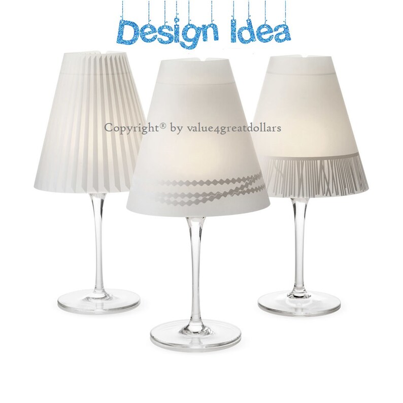 May include: Three white paper lampshades with different designs on wine glasses. The lampshades have a gray and white pattern, a gray fringe, and a pleated design.