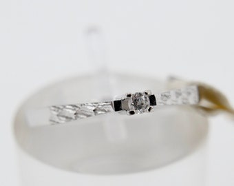 Puede incluir: Un anillo de plata con una sola piedra transparente engastada en el centro. El anillo está en un expositor blanco.