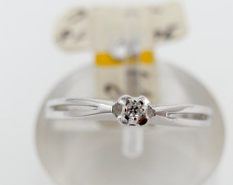 Puede incluir: Un anillo de plata con un solo diamante transparente engastado en el centro. El anillo se muestra en un soporte transparente.