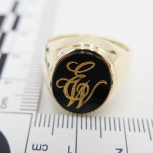 May include: A gold signet ring with a black oval stone featuring a gold engraved monogram of the letters "E & W".
