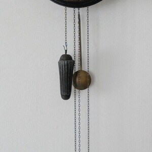 Peut inclure: Une horloge noire et dorée avec des chiffres romains et un pendule suspendu à des chaînes. L'horloge a un cadran noir avec des accents dorés et un fond blanc.