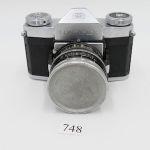 May include: A silver Contaxflex camera with a black leather body and a silver lens cap. The camera has a black dial with white markings.
