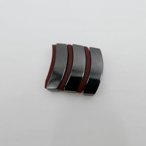 Könnte beinhalten: Fünf gebogene, schwarze Magnete mit roten Gummieinsätzen. Die Magnete sind übereinander gestapelt.