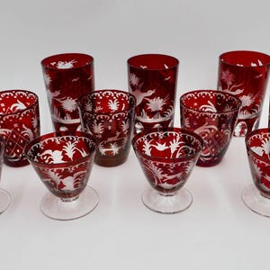 Pode incluir: Conjunto de 10 copos de vidro vermelho-rubi com desenhos florais gravados em branco. Os copos são de diferentes tamanhos e formas.