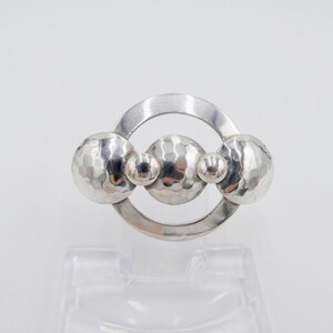 May include: A silver brooch with three hammered spheres and a circular frame.