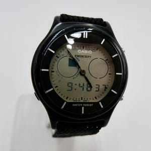 May include: Black Casio Twincept watch with a digital display showing the time as 9:48:37. The watch has a black strap and a round face with white markings.