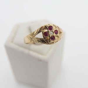 Op de afbeelding: Een gouden ring met een kruisontwerp bezet met rode en witte stenen.