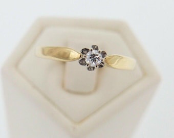 Op de afbeelding: Een gouden ring met een enkele ronde diamant gezet in een bloemvormige halo van kleinere diamanten.