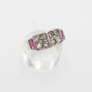 Op de afbeelding: Een zilveren ring met een vierkante zetting met meerdere kleine diamanten en twee roze rechthoekige stenen.