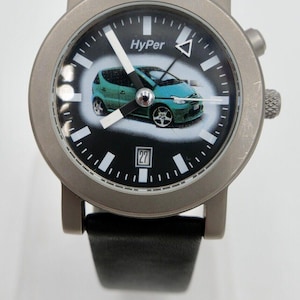 Könnte beinhalten: Eine silberne Armbanduhr mit schwarzem Zifferblatt und schwarzem Lederarmband. Das Zifferblatt der Uhr zeigt ein grünes Auto und das Wort "HyPer". Das Datumsfenster zeigt die Zahl 27.