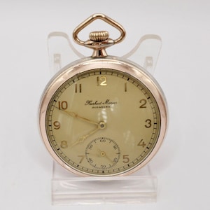 Op de afbeelding: Een gouden zakhorloge met een witte wijzerplaat en zwarte wijzers. Het horloge heeft Romeinse cijfers als uurmarkeringen en een kleine secondewijzer. De wijzerplaat van het horloge zegt "Robert Maurer Augsburg".