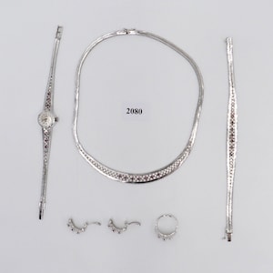 May include: A silver jewellery set with a watch, necklace, bracelet, earrings, and a ring. The jewellery features a delicate design with small, clear stones.