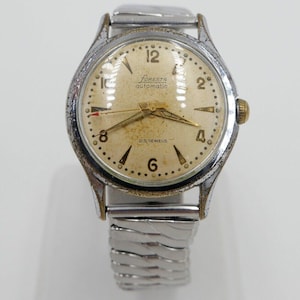May include: A silver wristwatch with a silver metal strap. The watch face is white with black markings and the text "Foresta automatic 25 jewels".