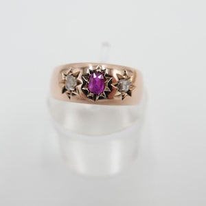 Op de afbeelding: Een gouden ring met een robijn en twee diamanten gezet in stervormige settings.