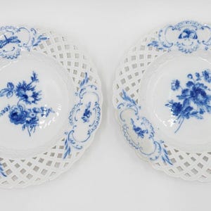 May include: Two white porcelain plates with blue floral designs and openwork lattice edges.