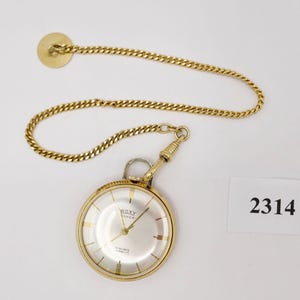May include: Gold pocket watch with a white face and black Roman numeral hour markers. The watch has a gold chain attached to it. The watch face says "ROXY SWISS 17 RUBIS SHOCKPROOF".