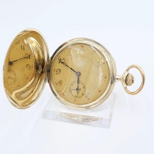 May include: A gold pocket watch with a white face and black hands. The watch has a round case and a chain attached to the top. The watch is open and the inside of the case is visible.