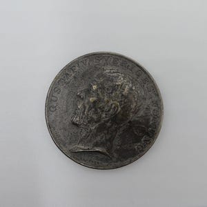 Puede incluir: Una moneda de plata con el perfil de un hombre en un lado y el texto "GUSTAFV SVERIGES KONING" en el otro.