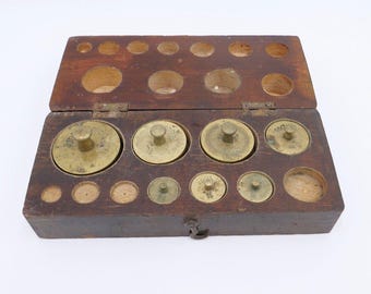 May include: A vintage wooden box with a hinged lid, housing a collection of brass weights. The box is a dark brown colour, and the weights are of different sizes. The box is open, displaying the weights in their compartments.