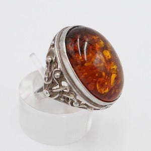 Könnte beinhalten: Ein silberner Ring mit einem ovalen Bernstein, der in einem filigranen Design gefasst ist.
