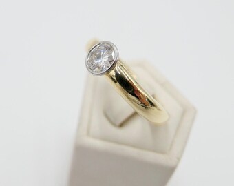 May include: A gold and white ring with a single round diamond set in a bezel setting.