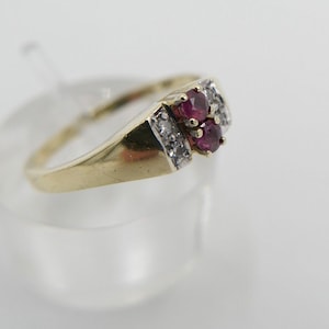 May include: A gold ring with two red ruby stones and smaller white diamonds set in a band.