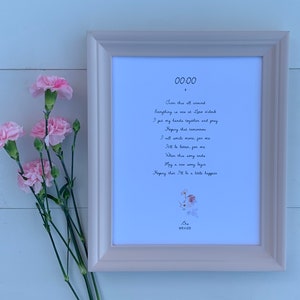 Puede incluir: Una impresión enmarcada con borde blanco presenta texto manuscrito y una ilustración floral. El texto incluye la hora "00:00" y un poema. Claveles rosas están dispuestos a la izquierda del marco, agregando un toque de color.