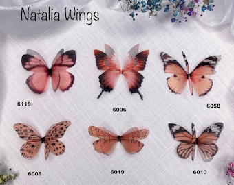 May include: Six different butterfly wing designs in shades of pink and brown. The wings are made of sheer fabric and have a delicate, feminine look. The designs are numbered 6005, 6006, 6010, 6019, 6058, and 6119.