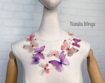 Op de afbeelding: Een delicate ketting met een waterval van gelaagde, doorschijnende vlinder vleugels in tinten roze, paars en wit. De vlinders zijn in een vloeiende, asymmetrische vorm gerangschikt, wat een speelse en etherische uitstraling creëert. De ketting is perfect om elke outfit een vleugje elegantie en speelsheid te geven.
