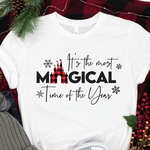 May include: White t-shirt with a red and black plaid castle graphic and the text "It's the most magical time of the year".