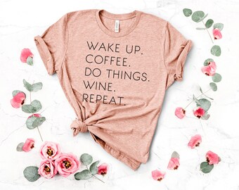 Puede incluir: Una camiseta marrón claro con el texto "WAKE UP. COFFEE. DO THINGS. WINE. REPEAT." impreso en negro.