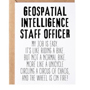 May include: A white card with black text that reads "GEOSPATIAL INTELLIGENCE STAFF OFFICER" and a humorous description of the job. The text reads "MY JOB IS EASY. IT'S LIKE RIDING A BIKE. BUT NOT A NORMAL BIKE. MORE LIKE A UNICYCLE CIRCLING A CIRCUS OF CHAOS, AND THE WHEEL IS ON FIRE!"