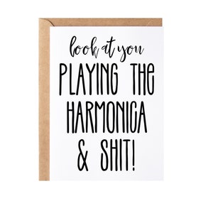 May include: A greeting card with a white front and a brown envelope. The card features black text that reads "look at you PLAYING THE HARMONICA & SHIT!"