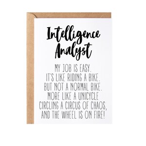 May include: A white card with black text that reads "Intelligence Analyst" and a humorous description of the job: "My job is easy. It's like riding a bike. But not a normal bike. More like a unicycle circling a circus of chaos, and the wheel is on fire!"