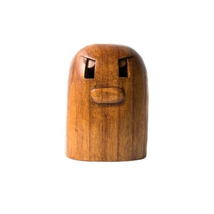 May include: A wooden figurine with a carved face, featuring two eyes and a mouth. The figurine is brown and has a smooth, polished finish.