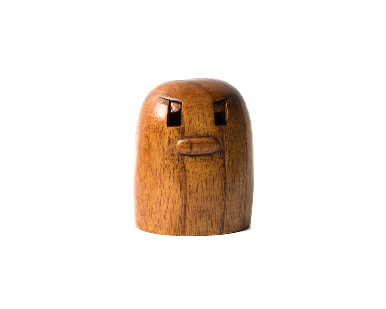 May include: A wooden figurine with a carved face, featuring two eyes and a mouth. The figurine is brown and has a smooth, polished finish.