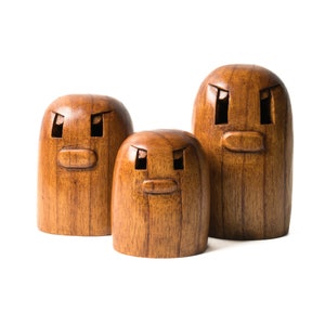 May include: Three wooden figurines with carved faces. The figurines are brown and have a wood grain texture. The faces have two eyes, a nose, and a mouth.