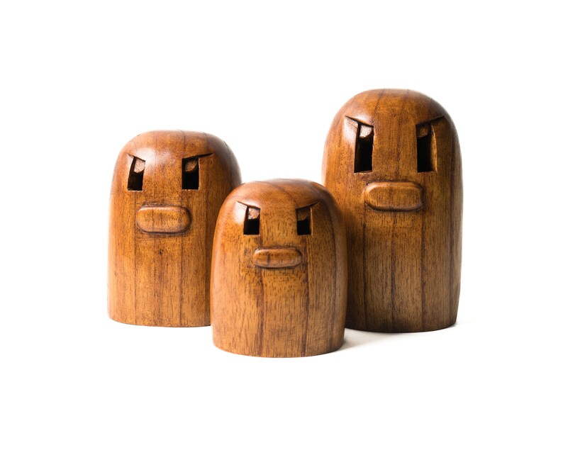 May include: Three wooden figurines with carved faces. The figurines are brown and have a wood grain texture. The faces have two eyes, a nose, and a mouth.