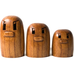 May include: Three wooden figurines with carved faces. The figurines are brown and have a simple design. The largest figurine is on the left, the middle figurine is in the center, and the smallest figurine is on the right.