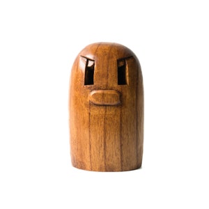 May include: A wooden figurine with a carved face, featuring two eyes and a mouth. The figurine is brown and has a smooth, polished finish.