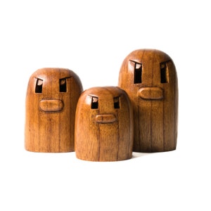 May include: Three wooden figurines with carved faces. The figurines are brown and have a simple, rounded shape. The largest figurine is in the back, and the smallest is in the front.