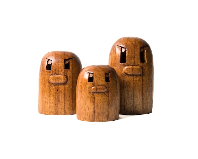 May include: Three wooden figurines with carved faces. The figurines are brown and have a simple, rounded shape. The largest figurine is in the back, and the smallest is in the front.