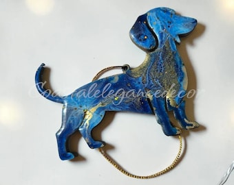 May include: A dachshund-shaped ornament featuring a marbled blue and gold finish with a glossy surface. The dog figure has a curled tail and is attached to a thin gold hanging cord. The text "coastalegancedeco" is visible across the center.