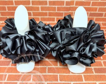 May include: A pair of black satin ruffle leg warmers. The leg warmers are made of soft, stretchy satin and have a ruffled design. They are perfect for adding a touch of elegance to any outfit.