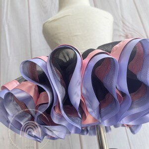 May include: A black tulle tutu skirt with layers of pink and lavender satin ribbon. The skirt is on a white dress form.