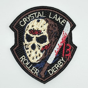 May include: Embroidered patch with a black border featuring a hockey mask, a bloody machete, and the text "CRYSTAL LAKE ROLLER DERBY 13". The patch has a beige mask, brown hair, and a white and red blade.