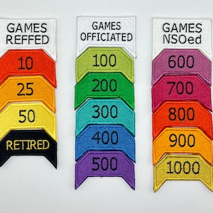 Może przedstawiać: Zestaw dziesięciu kolorowych naszywek haftowanych z białymi obwódkami. Naszywki są ponumerowane od 10 do 1000 w odstępach co 100. Naszywki są oznaczone jako "Games Reffed", "Games Officiated" i "Games NSOed".