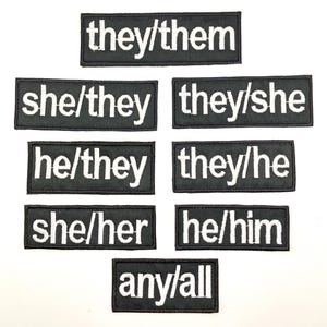 Może przedstawiać: Zestaw dziesięciu czarno-białych haftowanych naszywek do prasowania z różnymi kombinacjami zaimków, w tym "they/them", "she/they", "they/she", "he/they", "they/he", "she/her", "he/him" i "any/all".