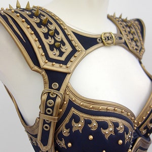 May include: A black and gold leather corset with a decorative design and spikes. The corset has a strap that goes over the shoulder and a buckle in the front.