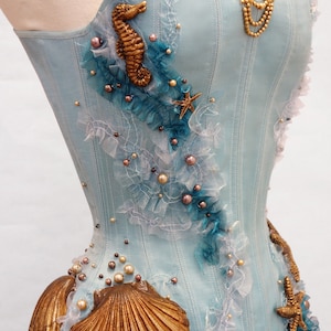 Puede incluir: Un cors&eacute; azul claro con un caballito de mar, conchas y estrellas de mar como adornos. El cors&eacute; est&aacute; decorado con perlas y encaje.